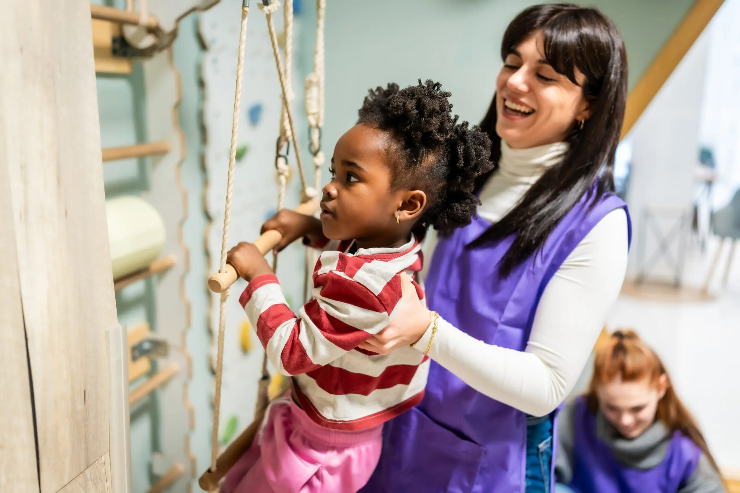 Young girl on indoor climbing equipment with adult support