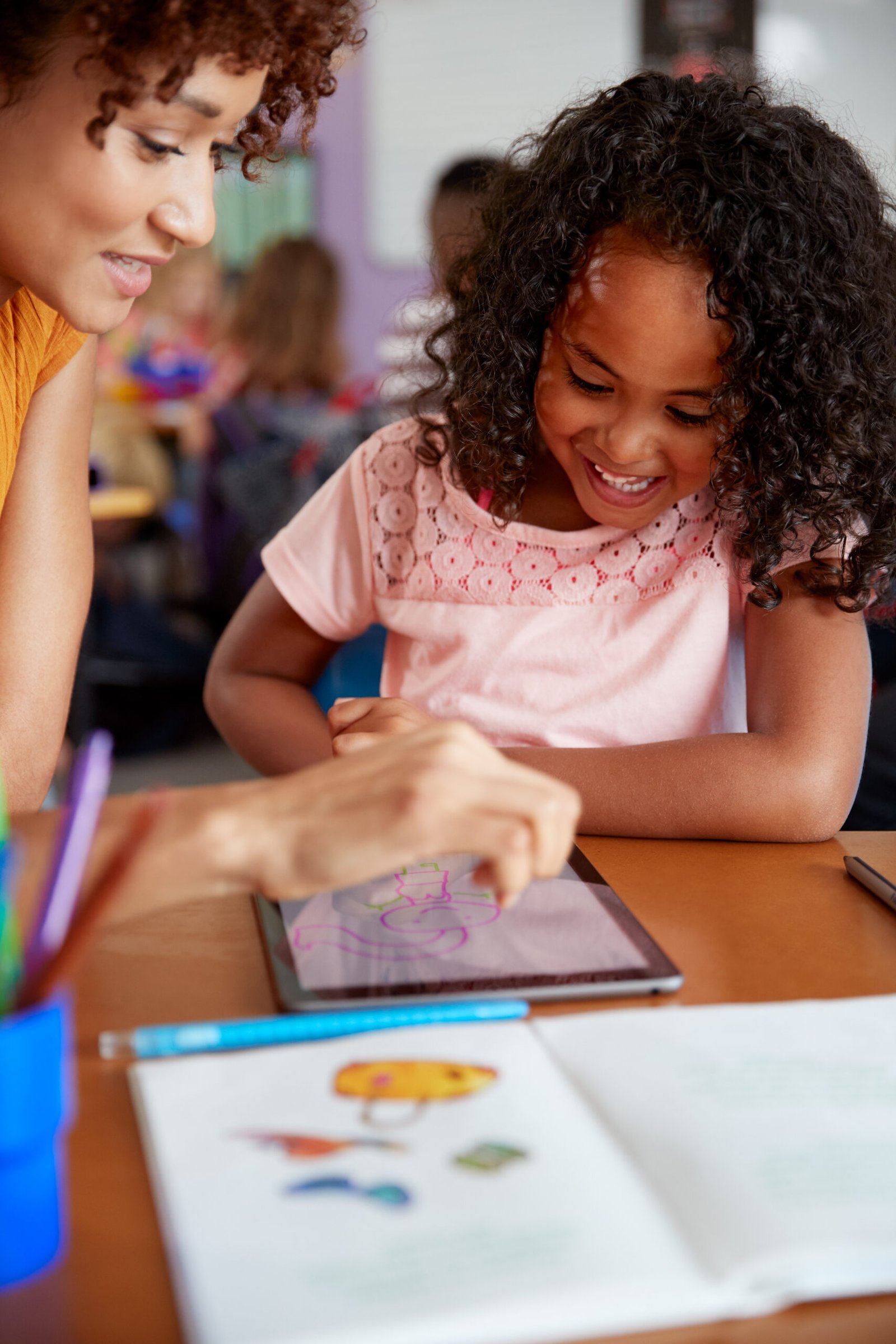 Elementary School Teacher And Female Pupil Drawing Using Digital Tablet In Classroom Elementary School Teacher And Female Pupil Drawing Using Digital Tablet In Classroom